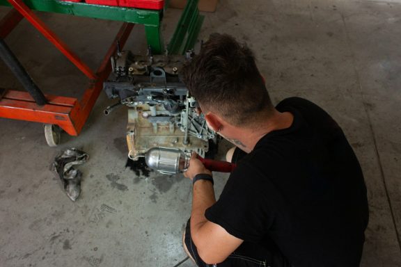 A person working on an engine in a workshop, surrounded by tools and parts.